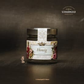 Honigglas mit Etikett von Schwarmgold auf Holzuntergrund